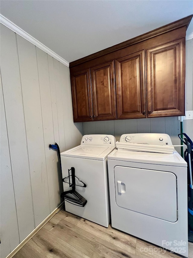 laundry room with ornamental molding, washing machine and dryer, cabinet space, and light wood-style floors