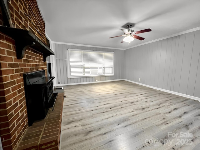 unfurnished living room featuring a ceiling fan, wood finished floors, a wood stove, and crown molding