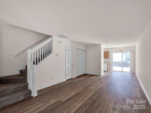 unfurnished living room with dark wood-type flooring, stairway, baseboards, and a chandelier