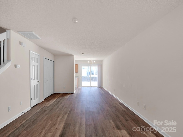 unfurnished room with visible vents, a notable chandelier, a textured ceiling, dark wood-style floors, and baseboards