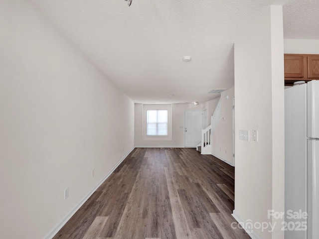 unfurnished living room with stairway, wood finished floors, baseboards, and a textured ceiling