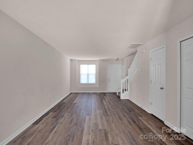 unfurnished living room with baseboards, a textured ceiling, dark wood-style floors, and stairs