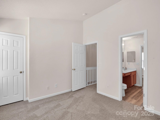 unfurnished bedroom featuring ensuite bath, lofted ceiling, baseboards, and light carpet