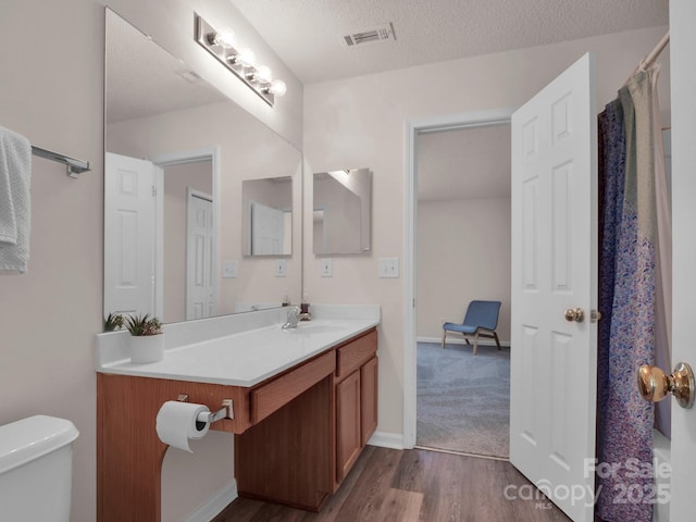 bathroom with vanity, wood finished floors, visible vents, a textured ceiling, and toilet