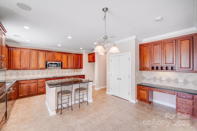 kitchen featuring a breakfast bar, a center island, built in desk, stainless steel microwave, and crown molding