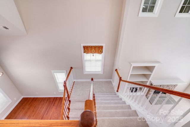 staircase with baseboards, a high ceiling, visible vents, and wood finished floors