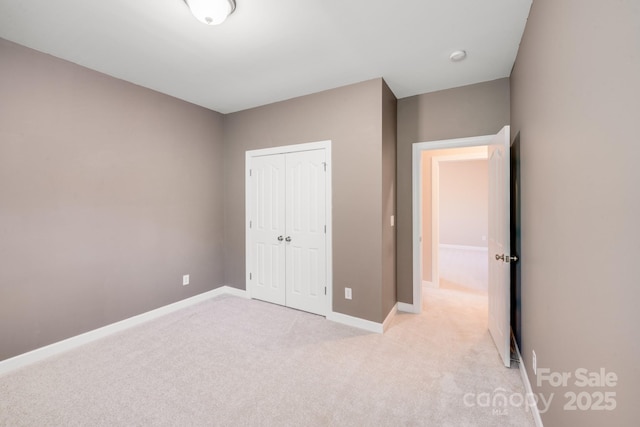 unfurnished bedroom with light carpet, a closet, and baseboards