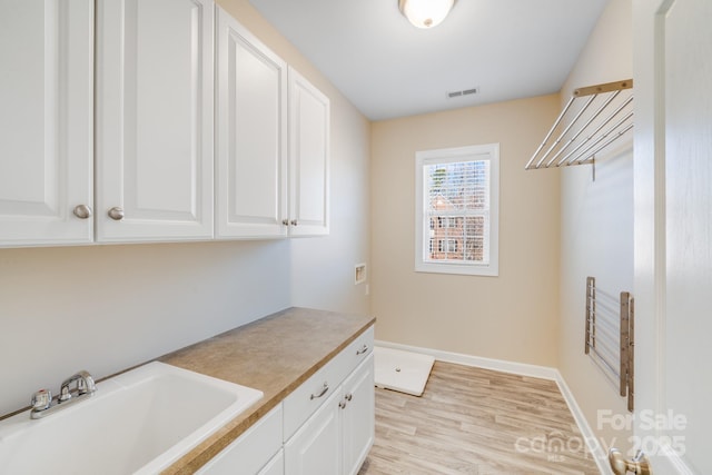 laundry room with hookup for a washing machine, a sink, visible vents, cabinet space, and light wood finished floors