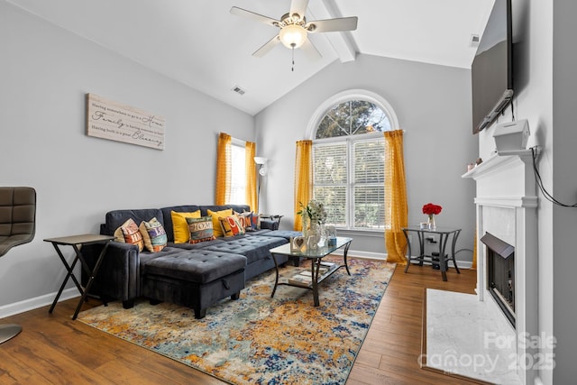 living area with lofted ceiling with beams, ceiling fan, a fireplace with flush hearth, visible vents, and hardwood / wood-style floors