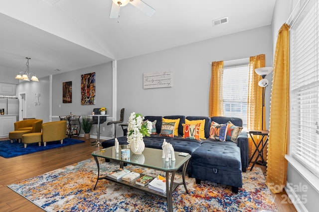 living room featuring ceiling fan with notable chandelier, visible vents, vaulted ceiling, and wood finished floors