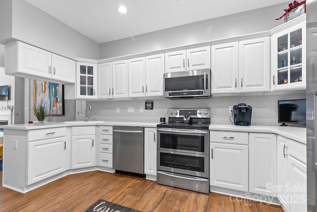 kitchen with stainless steel appliances, light countertops, white cabinets, wood finished floors, and a peninsula