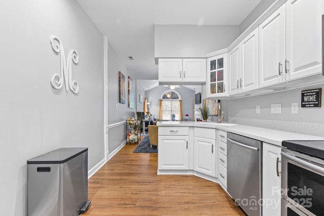 kitchen featuring light wood finished floors, white cabinets, glass insert cabinets, appliances with stainless steel finishes, and light countertops