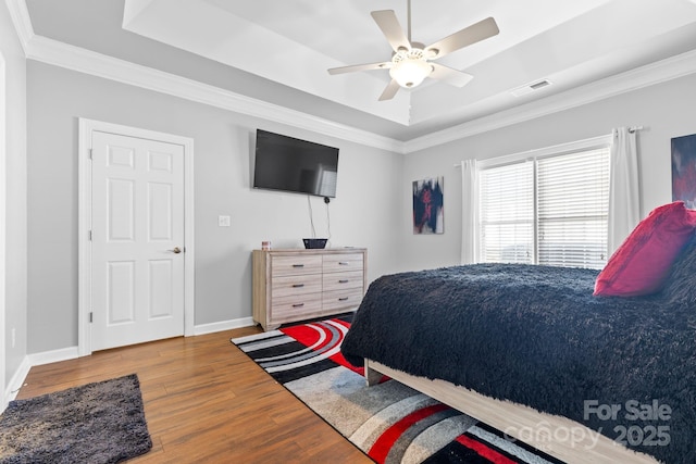 bedroom with baseboards, visible vents, a tray ceiling, and wood finished floors