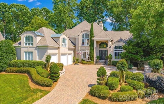 view of front facade with decorative driveway, french doors, a chimney, stucco siding, and an attached garage