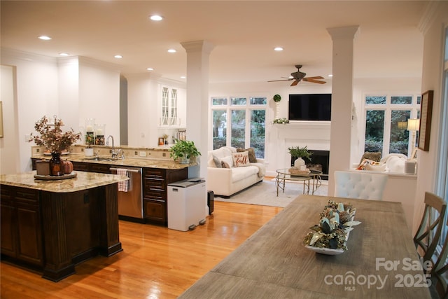 kitchen featuring stainless steel dishwasher, a sink, dark brown cabinetry, and ornate columns