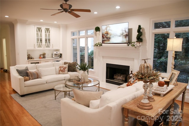 living area with recessed lighting, crown molding, wood finished floors, and a fireplace with flush hearth