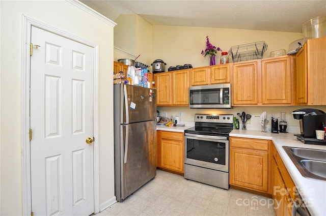 kitchen with a sink, stainless steel appliances, light countertops, lofted ceiling, and light floors