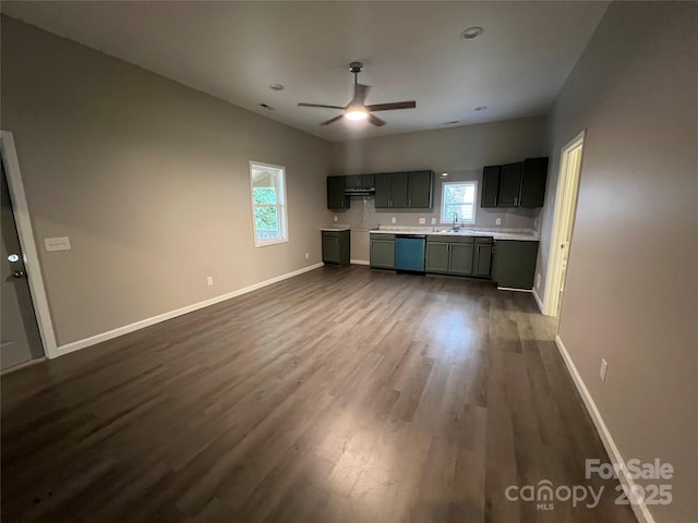 kitchen featuring dishwashing machine, dark wood finished floors, light countertops, a sink, and baseboards