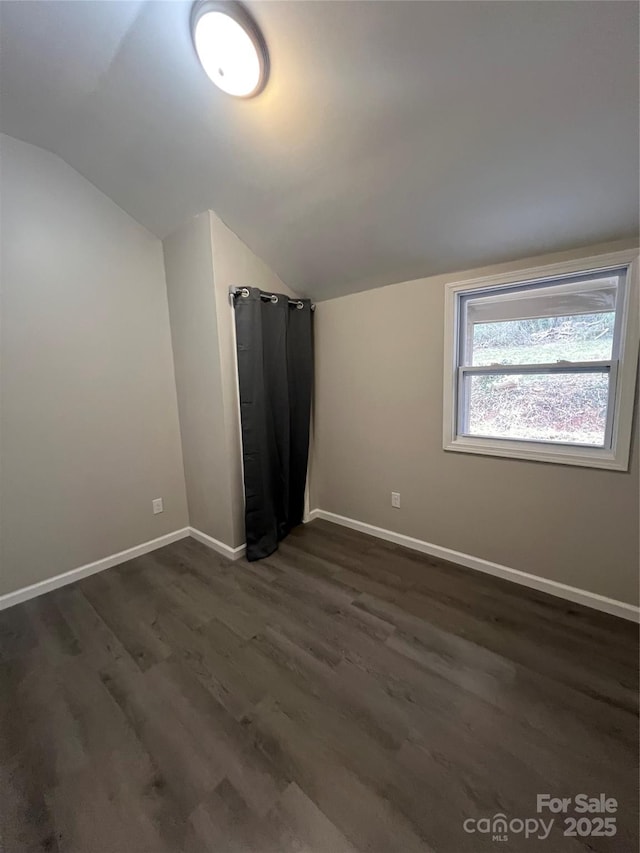 unfurnished room with vaulted ceiling, dark wood-style flooring, and baseboards