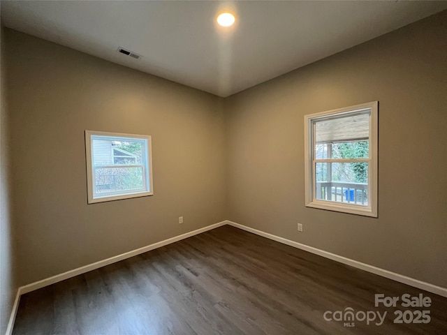 unfurnished room with dark wood-style floors, visible vents, and baseboards