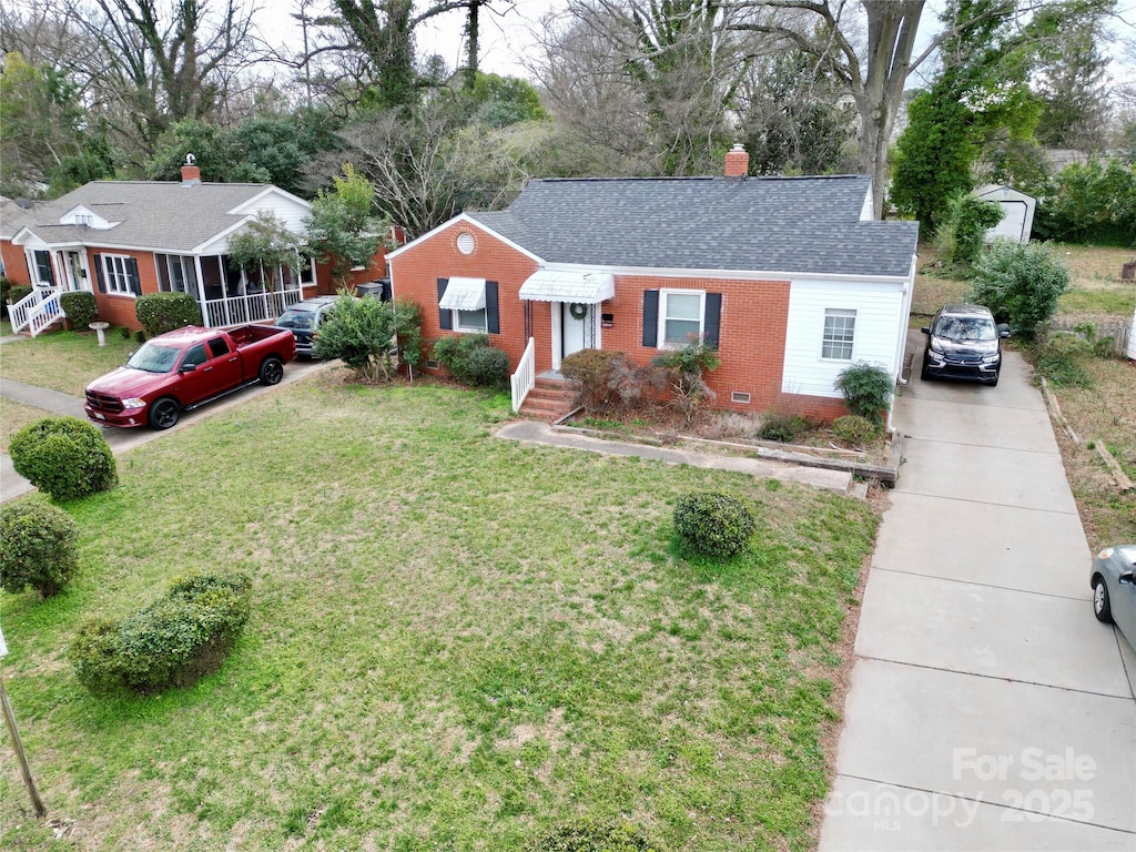 single story home with brick siding, roof with shingles, a chimney, driveway, and a front lawn