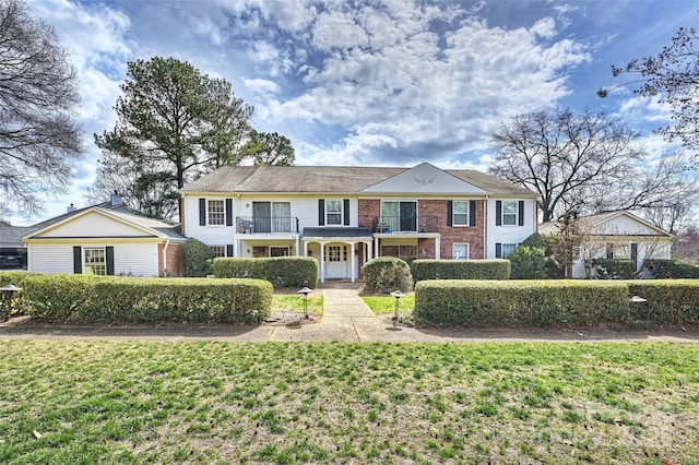 view of front of property featuring brick siding, a front lawn, and a balcony