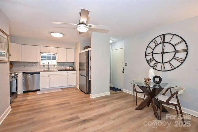 kitchen featuring stainless steel appliances, tasteful backsplash, light wood-style floors, white cabinets, and a sink