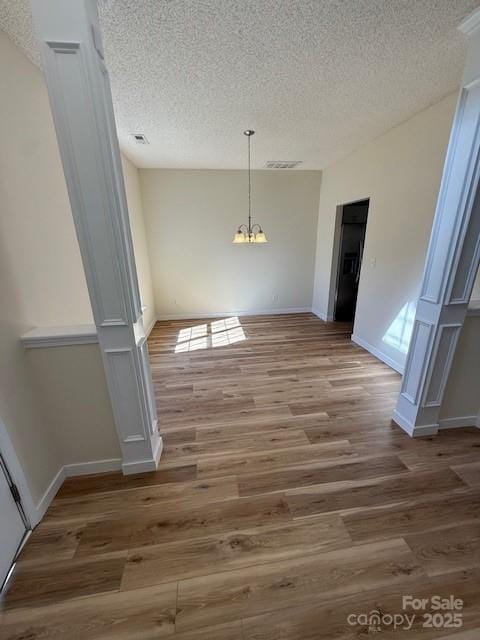 unfurnished dining area with a textured ceiling, light wood-style flooring, a notable chandelier, visible vents, and baseboards