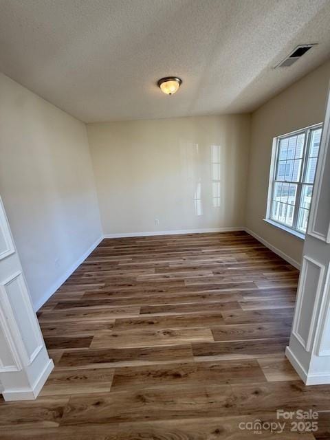 unfurnished room with a textured ceiling, wood finished floors, visible vents, and baseboards