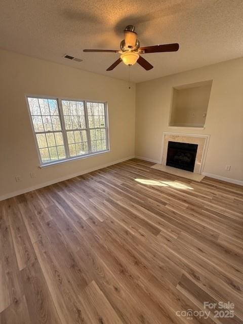 unfurnished living room with a textured ceiling, a fireplace, wood finished floors, and visible vents