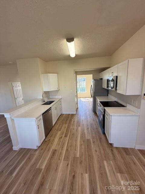 kitchen featuring light wood finished floors, appliances with stainless steel finishes, white cabinets, a sink, and a peninsula