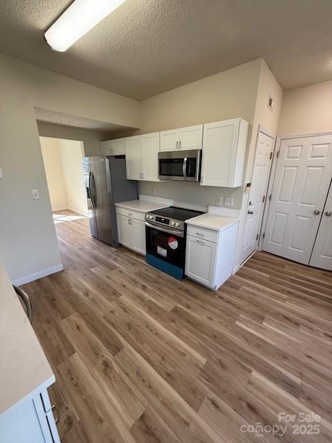 kitchen featuring stainless steel appliances, light countertops, white cabinetry, and wood finished floors