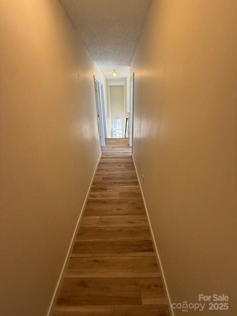 corridor with a textured ceiling, wood finished floors, and baseboards