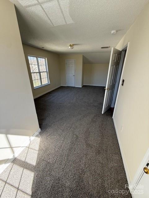 spare room with a textured ceiling, dark carpet, visible vents, and baseboards