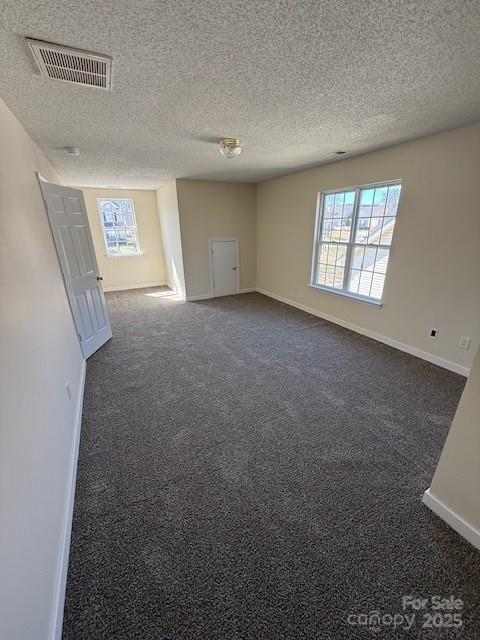 carpeted empty room featuring baseboards, visible vents, and a textured ceiling