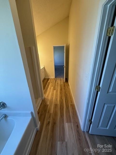 corridor with vaulted ceiling, wood finished floors, and baseboards