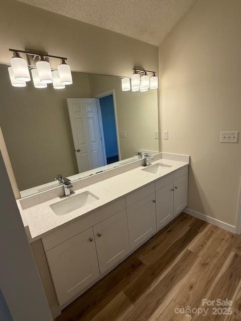 full bath with double vanity, a textured ceiling, a sink, and wood finished floors