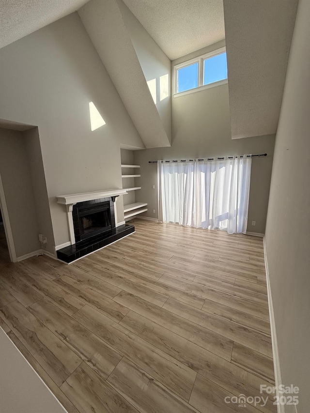 unfurnished living room featuring a tile fireplace, a textured ceiling, baseboards, and wood finished floors