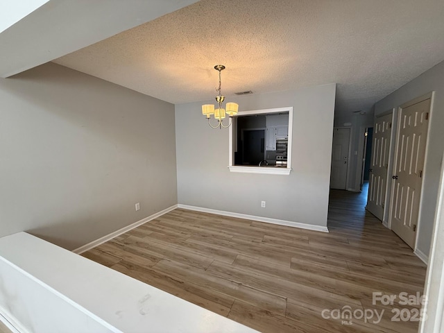 empty room with visible vents, baseboards, a notable chandelier, and wood finished floors