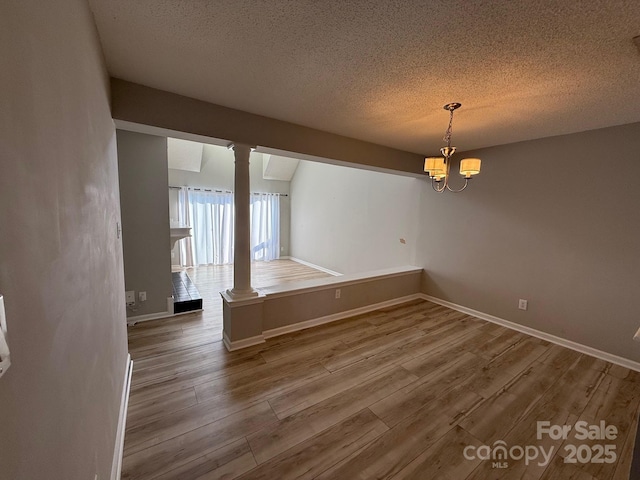 unfurnished dining area featuring a chandelier, wood finished floors, and ornate columns