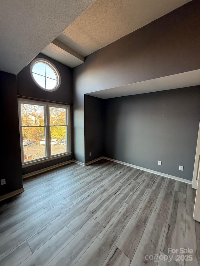 empty room featuring lofted ceiling, a textured ceiling, baseboards, and wood finished floors