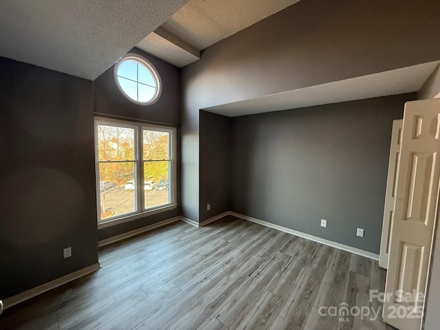 empty room with lofted ceiling, a textured ceiling, baseboards, and wood finished floors