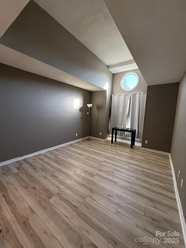 additional living space featuring vaulted ceiling, a textured ceiling, baseboards, and wood finished floors