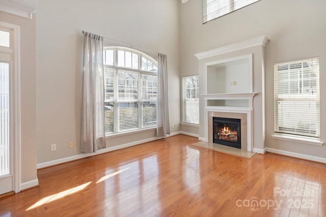 unfurnished living room featuring a fireplace, a towering ceiling, baseboards, and wood finished floors