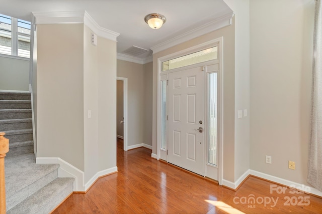 foyer entrance featuring baseboards, stairway, wood finished floors, and crown molding