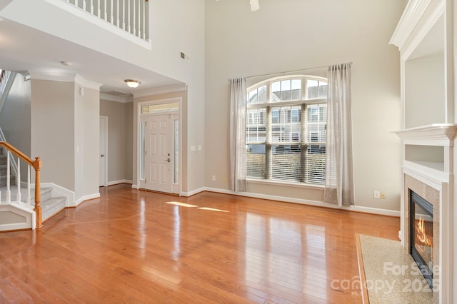 unfurnished living room featuring stairs, crown molding, a fireplace, baseboards, and hardwood / wood-style flooring