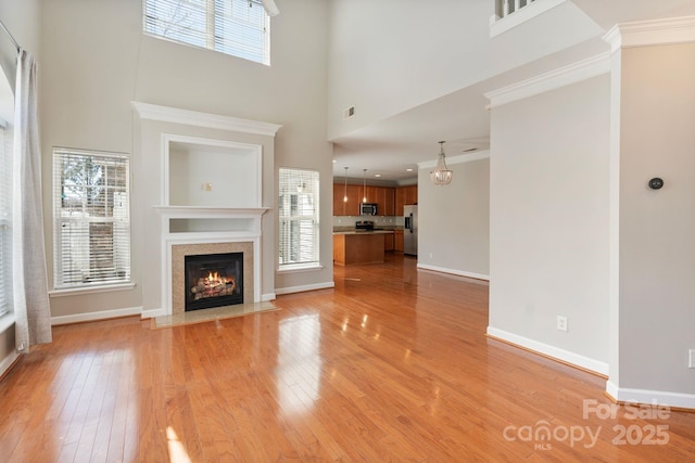 unfurnished living room with a high ceiling, a fireplace with flush hearth, baseboards, light wood-type flooring, and crown molding