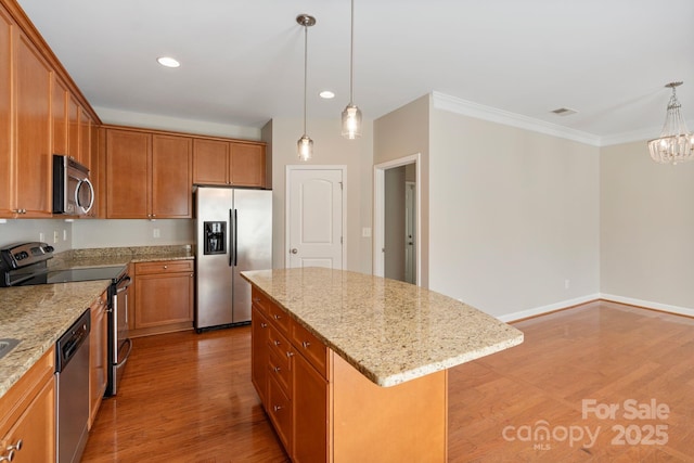 kitchen with appliances with stainless steel finishes, ornamental molding, light stone counters, a center island, and light wood-style floors