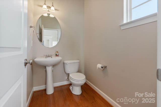 half bath featuring a sink, wood finished floors, toilet, and baseboards