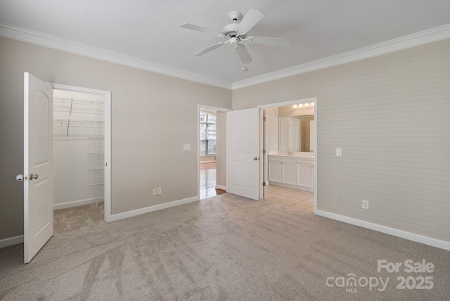 unfurnished bedroom with crown molding, baseboards, a walk in closet, and light colored carpet